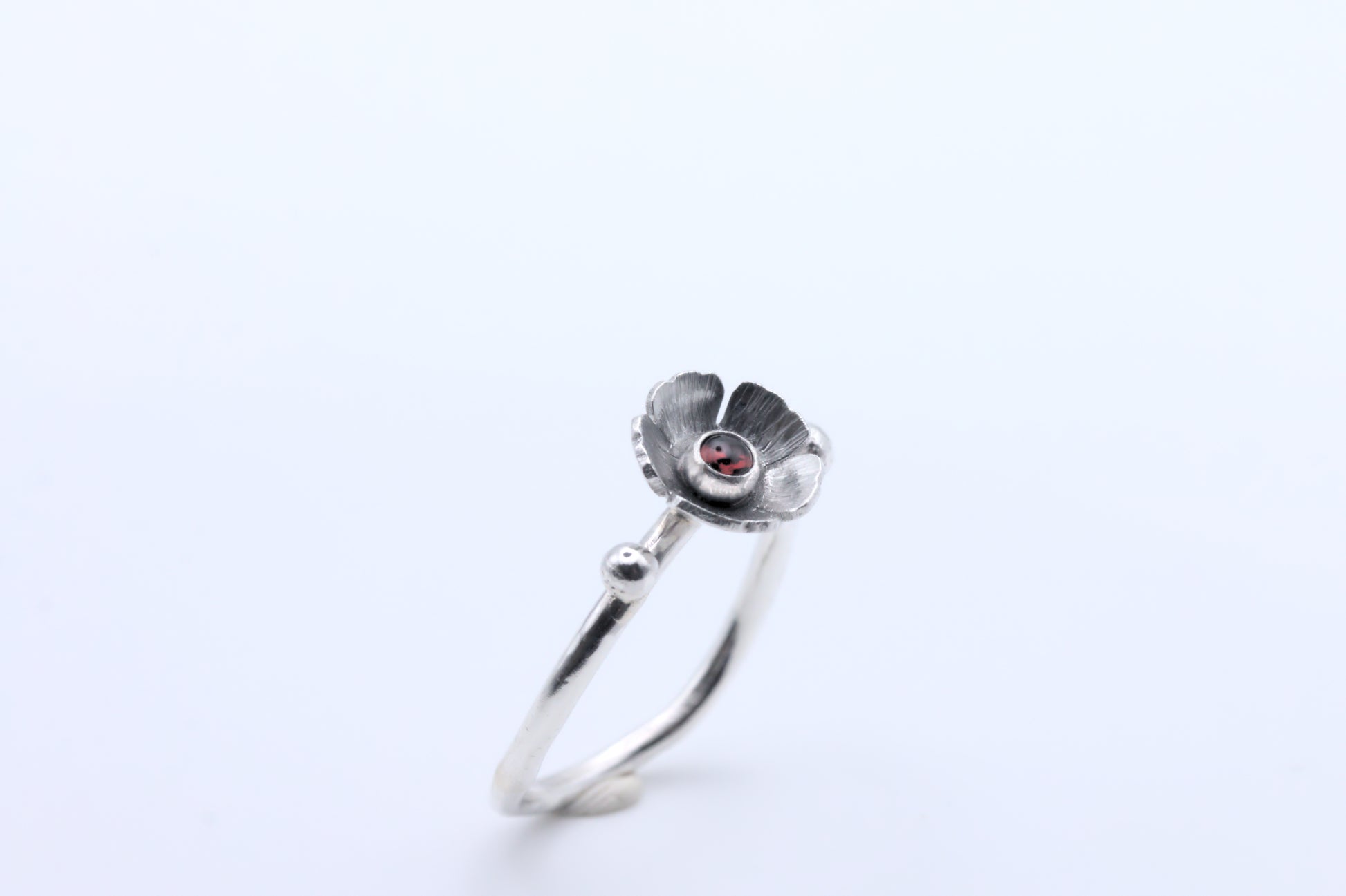 A garnet gemstone in a flower on a wavy silver ring band