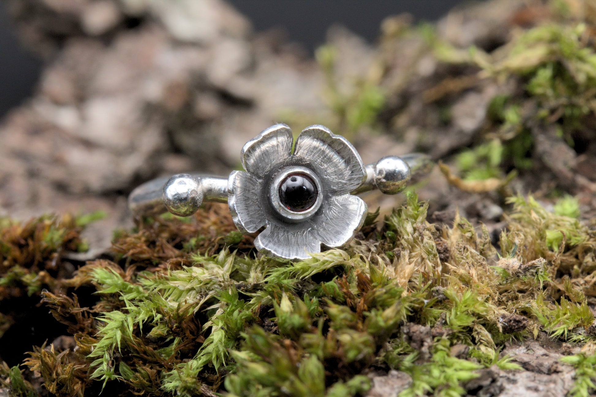 A garnet gemstone in a flower on a wavy silver ring band