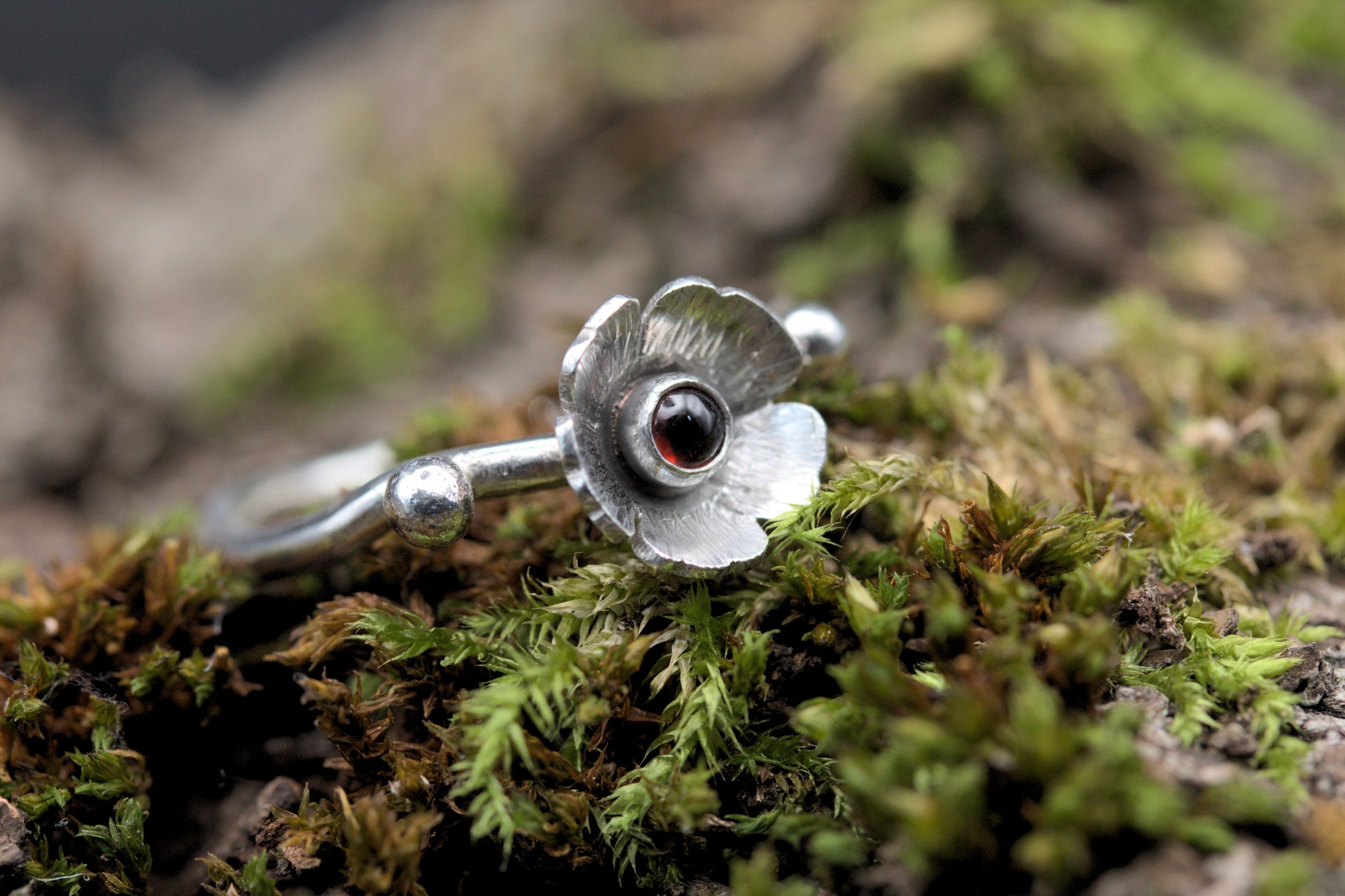 A garnet gemstone in a flower on a wavy silver ring band