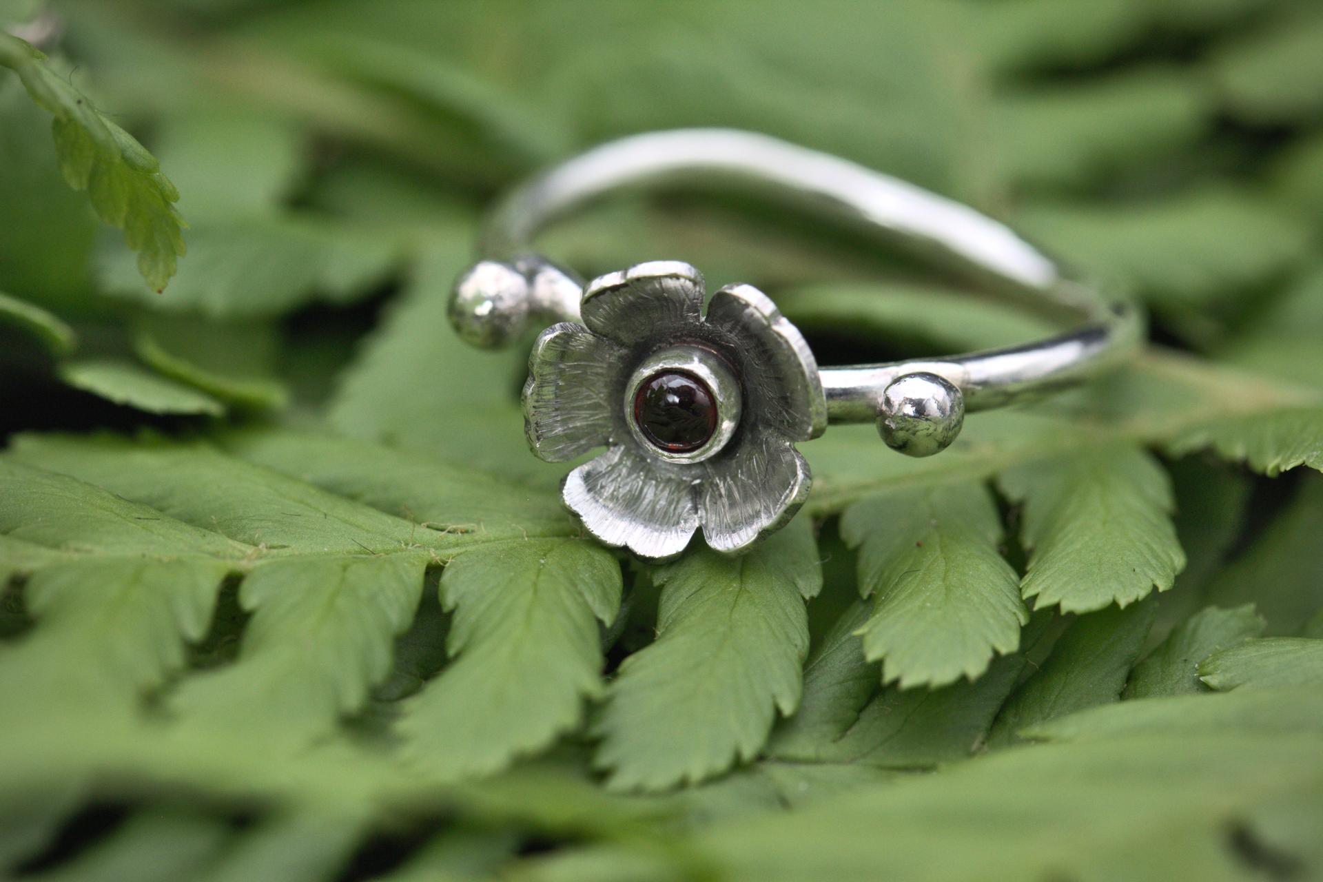 A garnet gemstone in a flower on a wavy silver ring band