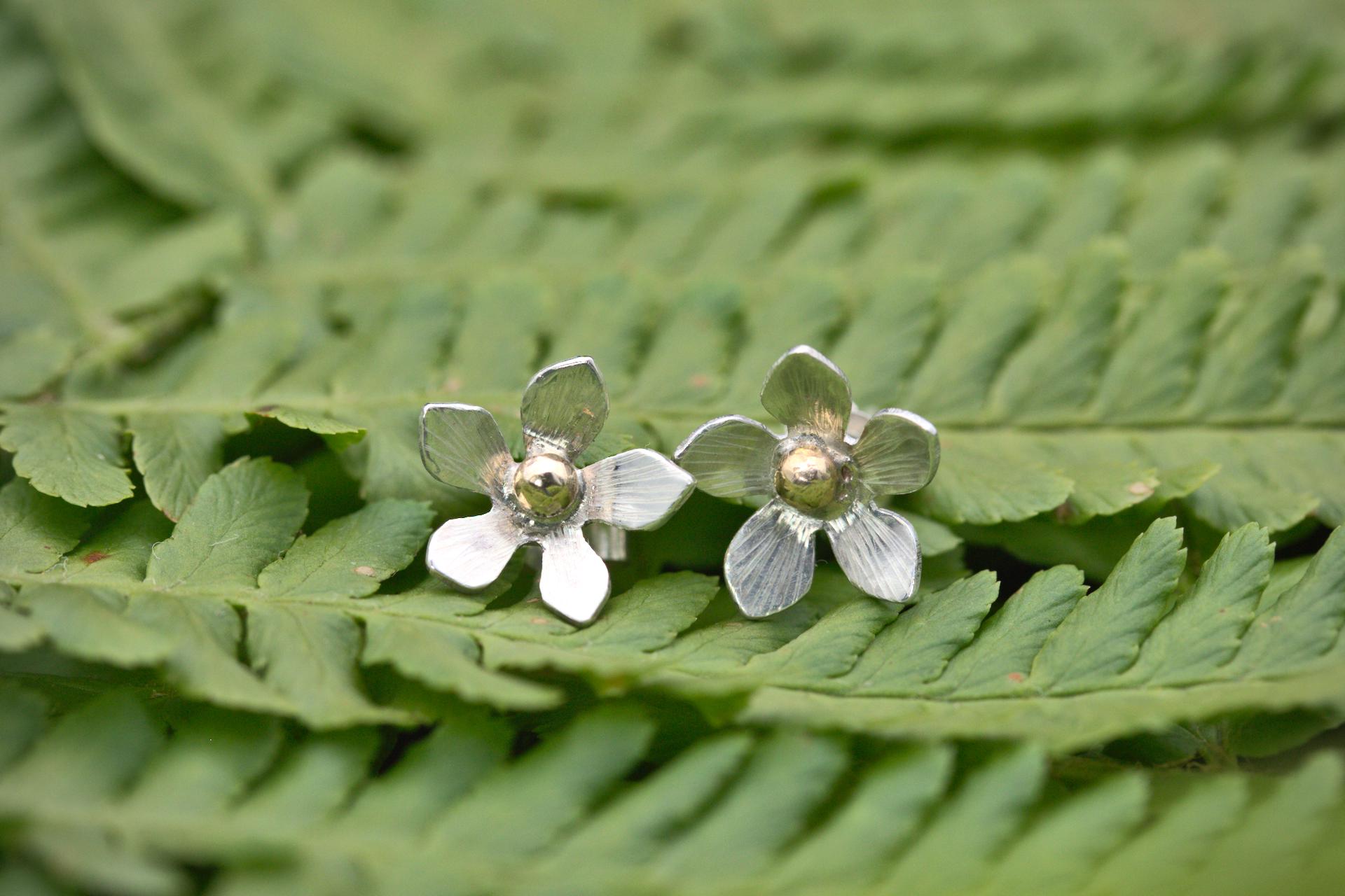 A silver flower stud earring with a gold bead in the centre